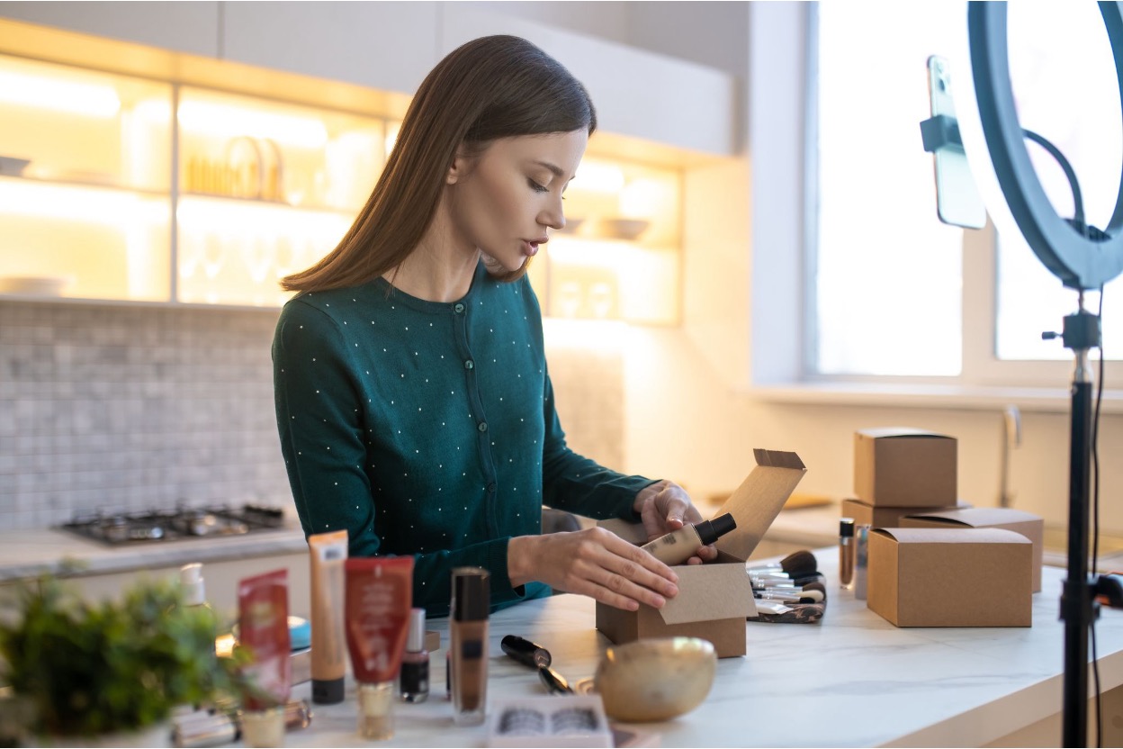 Young woman packing some products in front of a ring light and smartphone setup