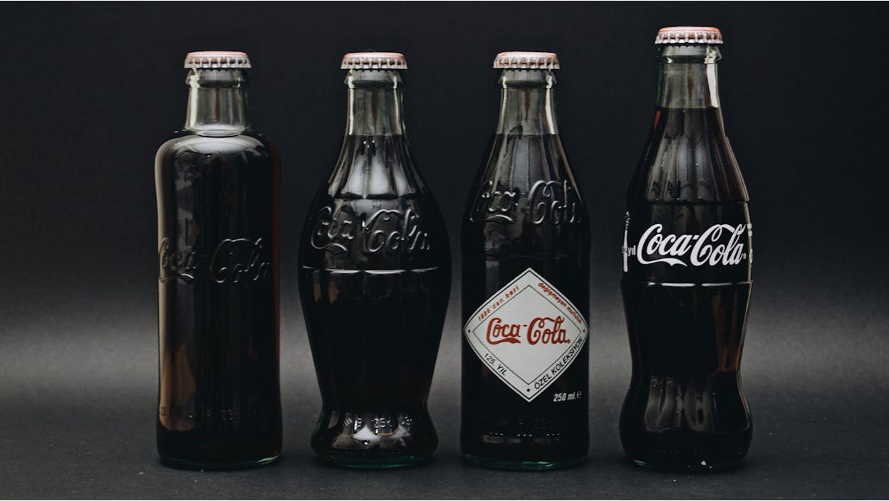 Different Coca-Cola glass bottles on a gray background showing the evolution of its design